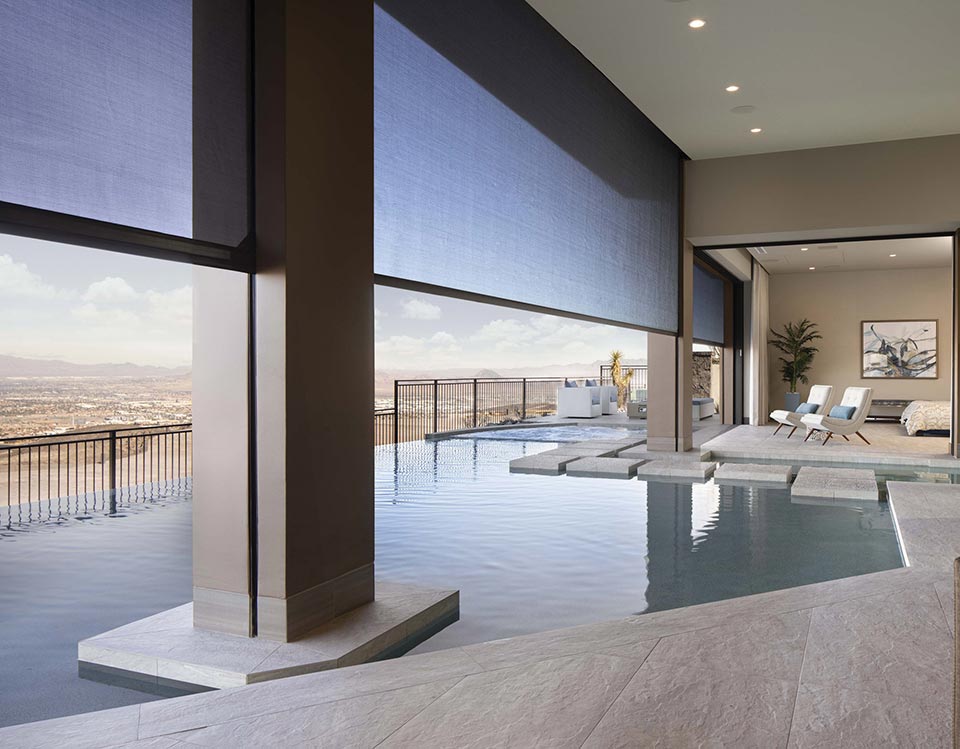 Modern covered patio with retractable shades lowered over an infinity pool, offering sun protection and privacy.