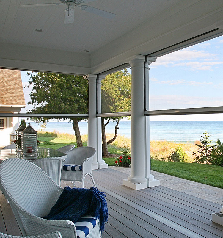 Coastal porch with white columns and retractable screens, featuring wicker furniture and ocean views across a manicured lawn