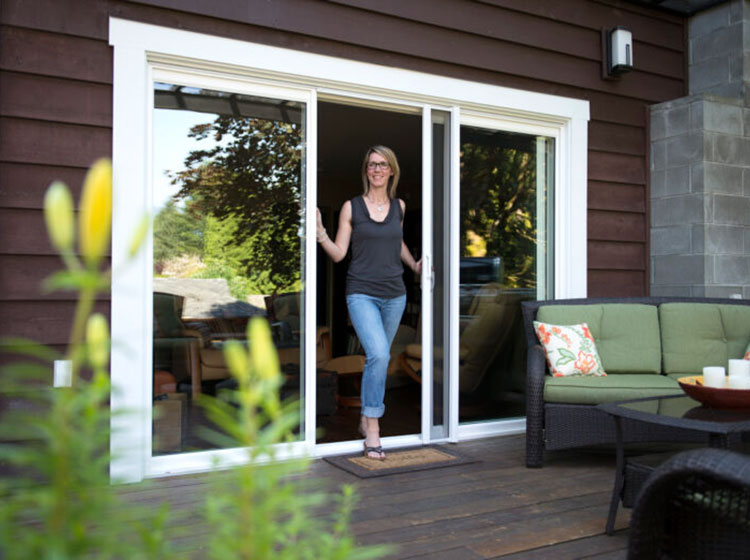 Woman standing in sliding glass door with retractable screen, outdoor patio with furniture visible through doorway