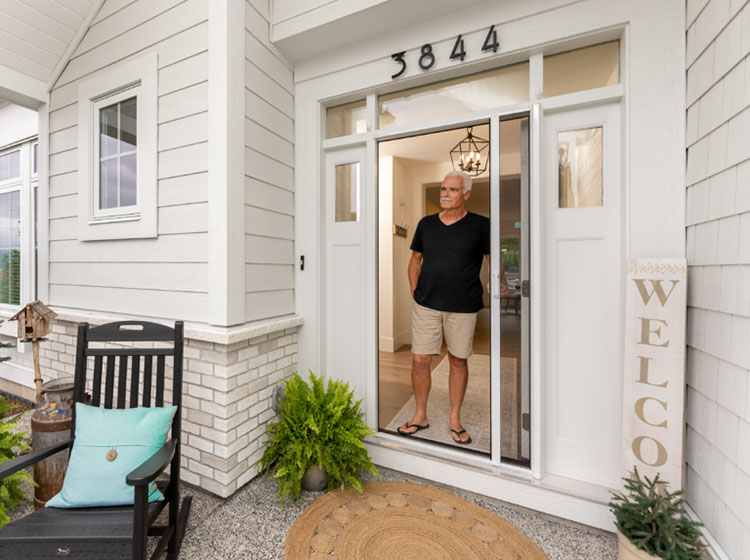 Person standing in doorway with a retractable screen door, showcasing discreet installation on modern white home entrance