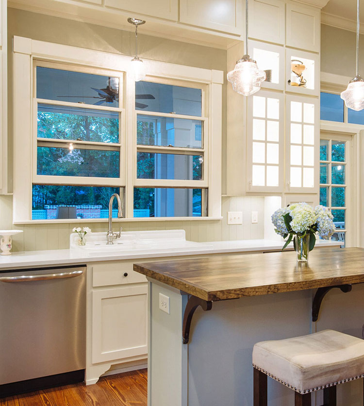 Bright kitchen with white cabinets and crystal pendant lights, featuring large windows with garden view